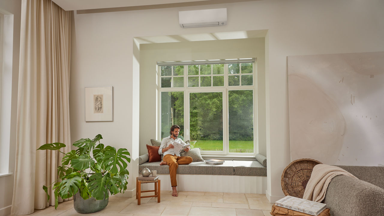 Daikin Sensira airco in een lichte woonkamer met man die leest bij het raam