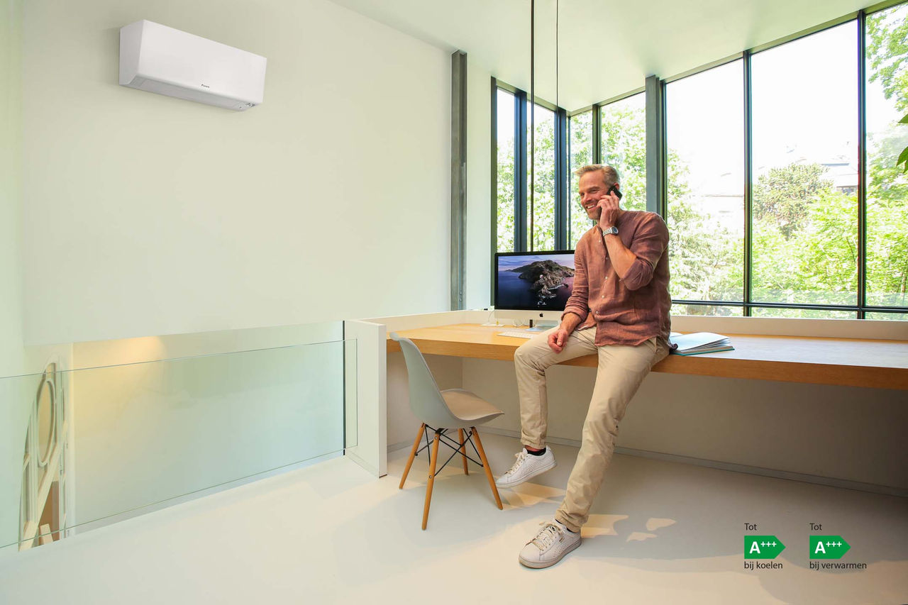 Man belt aan zijn bureau in een lichte werkruimte met airco aan de muur